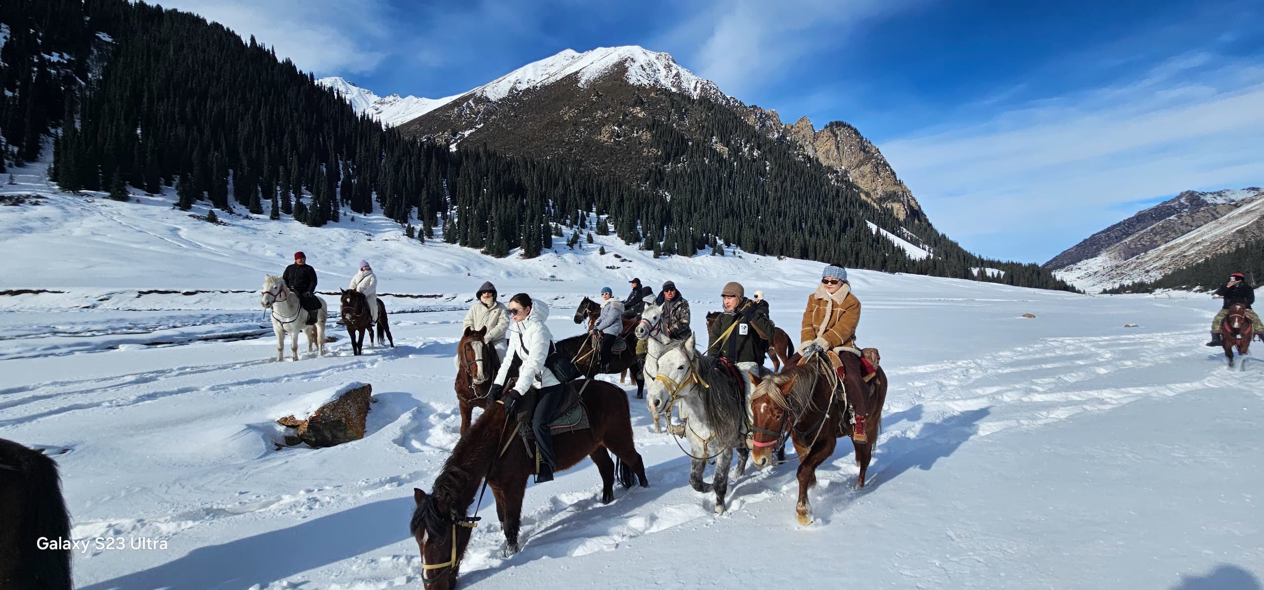 Photo of a group of people riding horses in snowy day with a mountain as a background